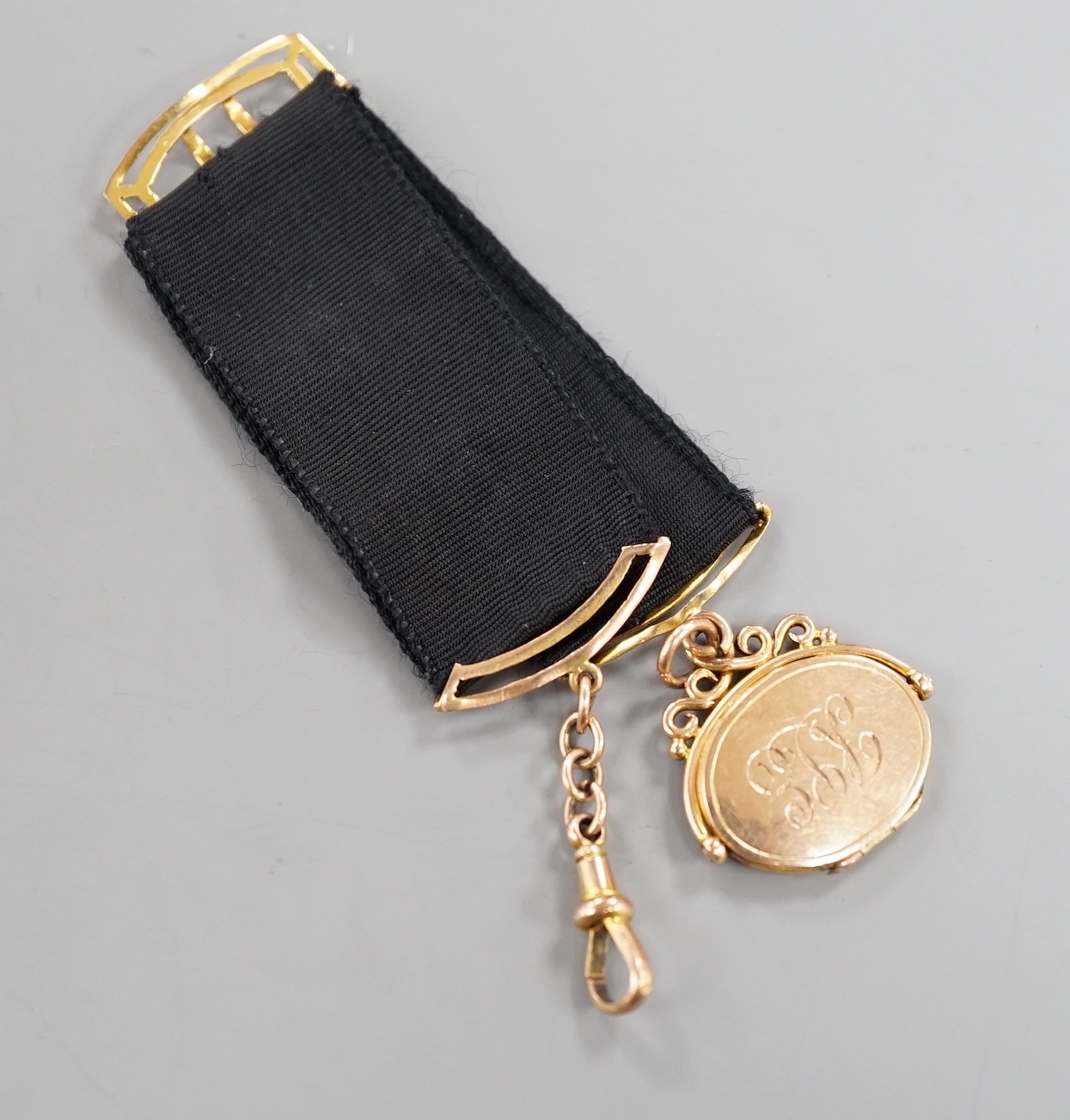 A Victorian yellow metal oval locket fob, hung from a yellow metal mounted black suspension sash, with later engraved date and initials.